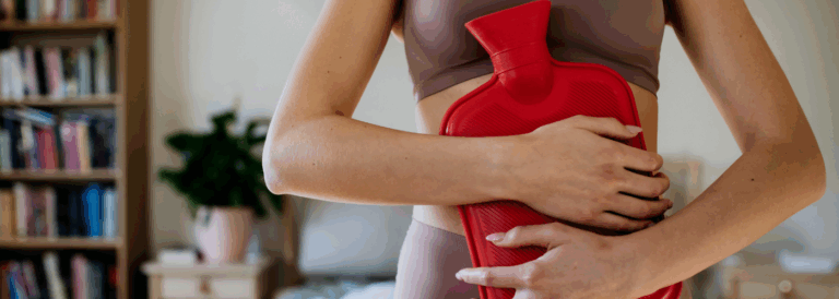 Mujer aplicando una bolsa de agua caliente sobre el abdomen para aliviar dolor pélvico, síntoma común de la adenomiosis.